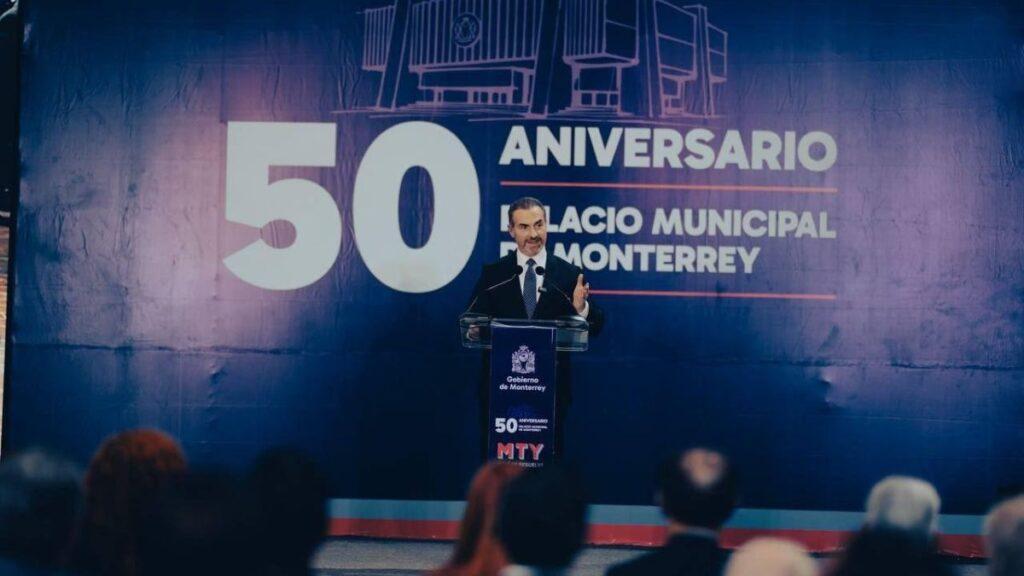 Man in a suit giving a speech at a podium during Monterrey’s 50th anniversary event, with a large blue backdrop reading '50 Aniversario' behind him.